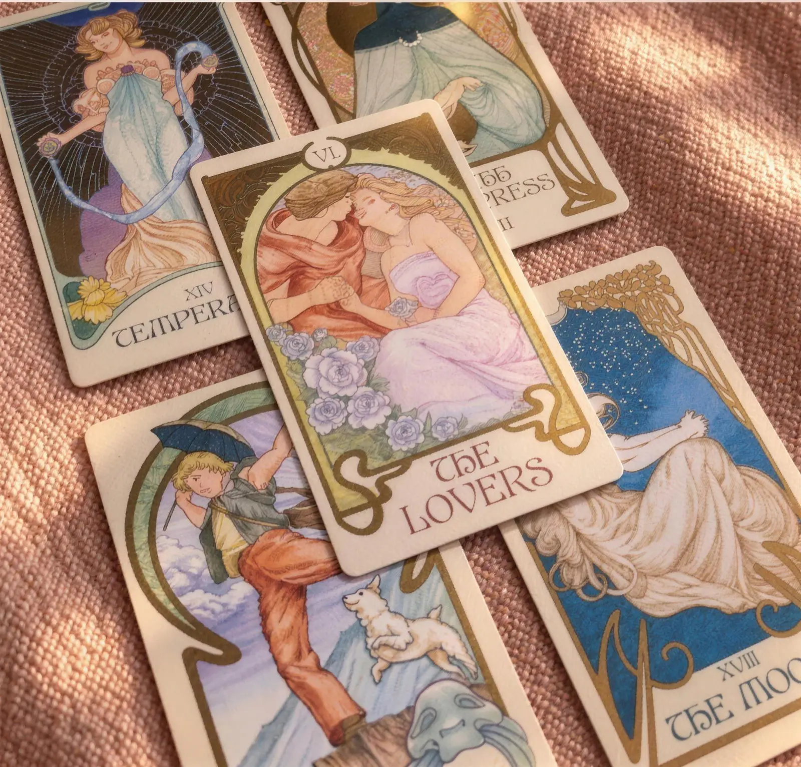 Cartas dos Arcanos Maiores espalhadas sobre um tecido rosa, com Os Enamorados ao centro.