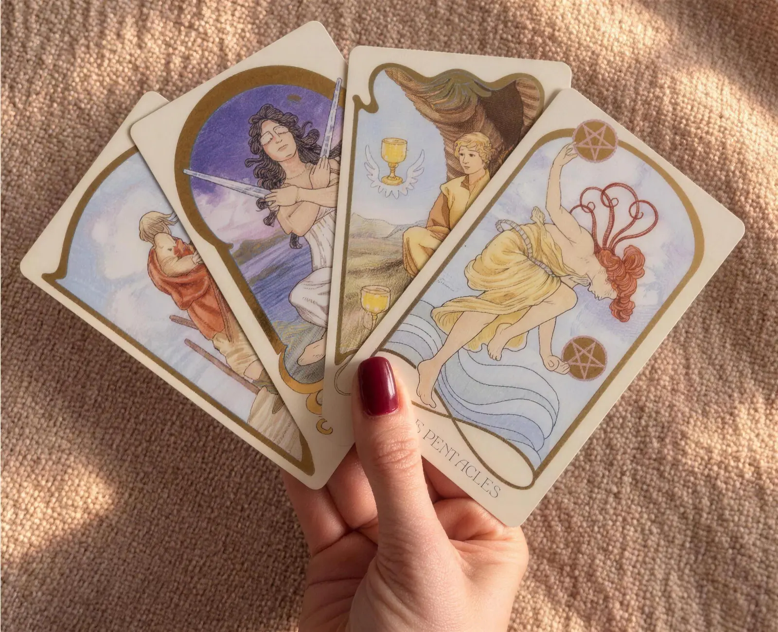 Mão segurando quatro cartas de tarô abertas em leque sobre um tecido claro.